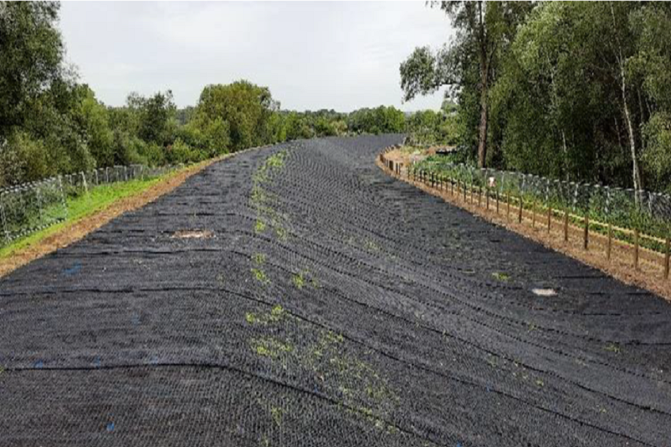 Image shows black matting on an embankment which stretches in a curve to the right between trees