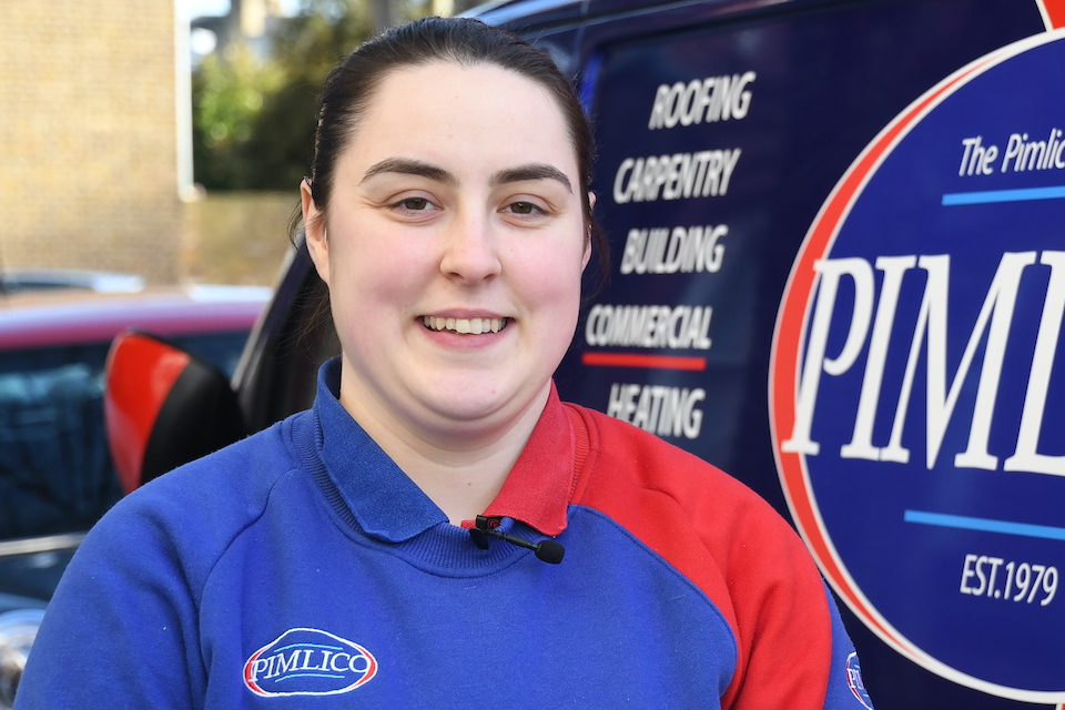 A photograph of Charlotte Muir, who is smiling and standing outside her workplace, Pimlico Plumbers. 
