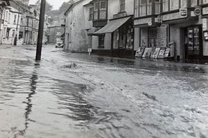 Черно-белое фото паводковых вод, протекающих по торговой улице в Бире, 1950-е годы.