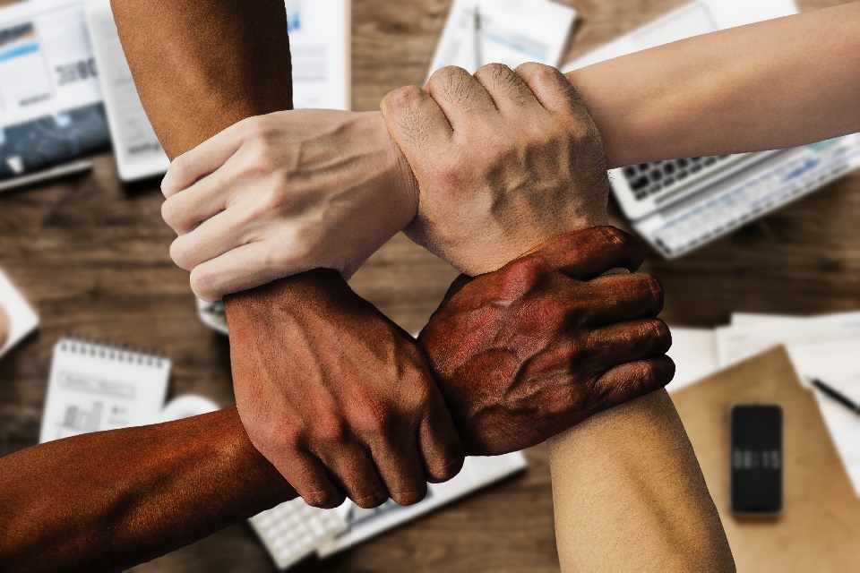 Four hands from different ethnic backgrounds holding another person's arm