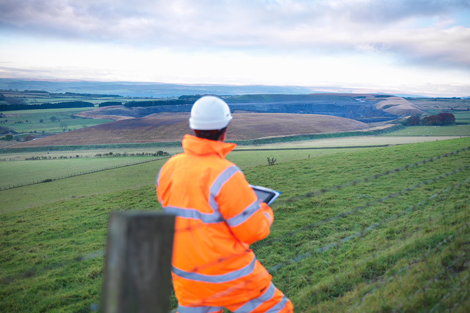 Worker in Hi Vis, looking out to the countryside whist holding a tablet 