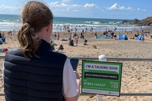 A young woman using her mobile phone to scan a QR code on a sign with a busy beach in the background