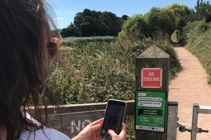 Woman using mobile phone to scan a QR code on a fence post