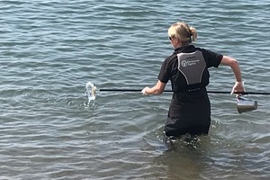 Female with lifejacket on up to waist in seawater taking a sample of the bathing water