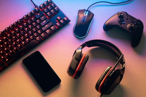 игровая клавиатура, гарнитура, компьютерная мышь, мобильный телефон и контроллер игровой приставки, разложенные на поверхности