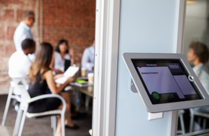 A picture of an electronic room booking display outside a meeting room full of people