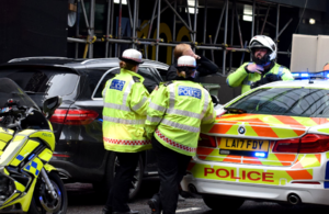 Three police officers standing next to patrol car in busy urban street