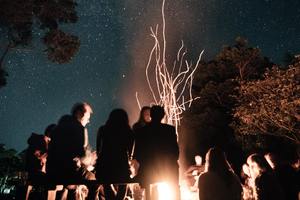 A group of people in silhouette gathered around a small fire at night