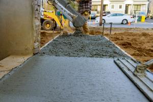 Строитель заливает железобетонный цемент для тротуара в новом жилом доме