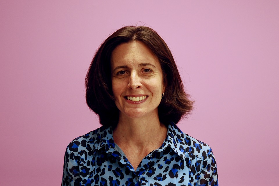 Photograph of Sarah Cardell stood in front of a pink wall.