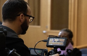 Video cameraman setting up equipment in front of woman in court building.