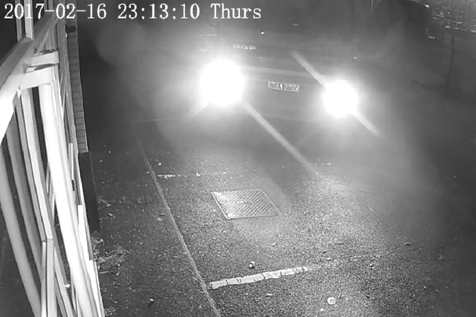 A black and white CCTV image shows the headlights of a lorry coming into view