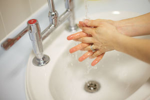 A person washing their hands in a basin under a running tap.