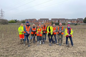 Volunteers with high vis jackets stood on land with newly planted trees behind
