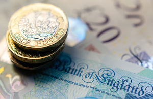 A photo of several British one pound coins piled on top of a five pound note, ten pound note and two twenty pound notes