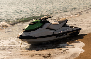 A powered watercraft sitting stationary on the sand at the beach at the edge of the water as the tide goes out
