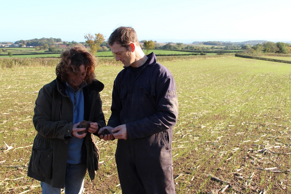 A woman and a man stood on a field examining soil samples in their hands.