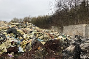 A pile of assorted carpet and wood waste. Woodland can be seen nearby.