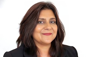 A headshot of Cindy smiling, a woman of colour with brown, shoulder-length hair and wearing a blazer