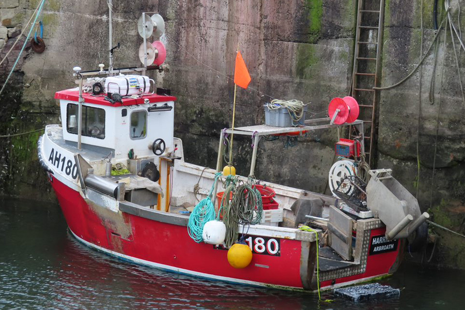 A side-on view of the creel fishing vessel Harriet J berthed against a harbour wall