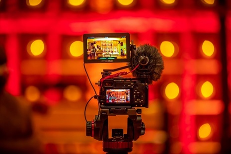 Photo depicting the creative industires. A video camera faces a red backdrop which has yellow lights. The video camera is filiming this backdrop. 
