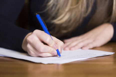 The hands of a student writing on an exam paper during an examination