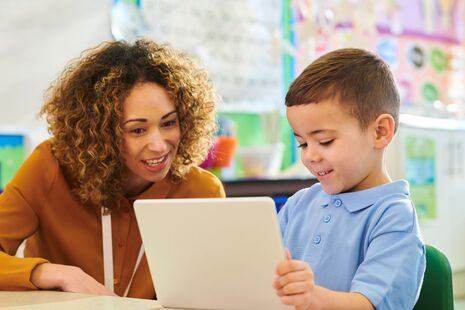 Female teacher and boy with tablet device in classroom setting