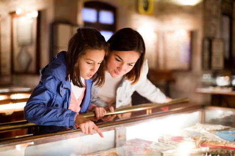 A woman and a young girl look together at a museum exhibit in a glass case