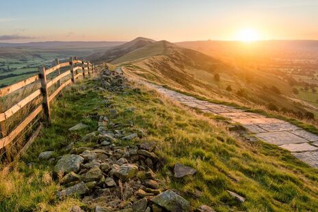 A stone footpath and wooden fence leading a long The Great Ridge in the English Peak District