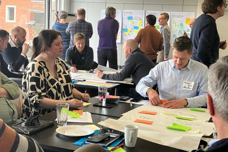 people sitting at desks and standing besides whiteboards in discussion