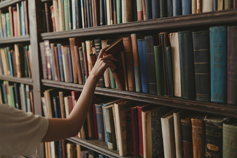 A person taking a book from a full book shelf.