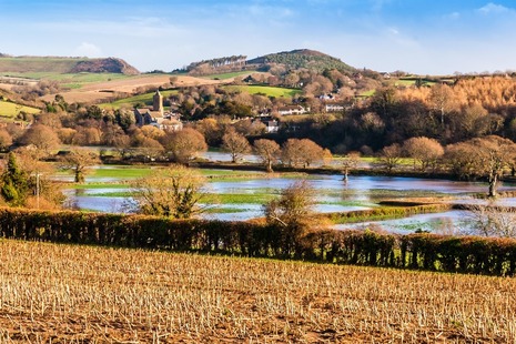 Photograph of an area of flooded countryide with a village and green hills in the distance.