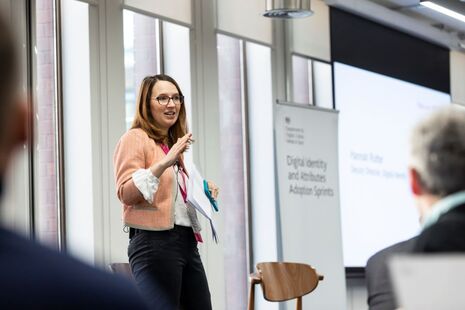 Hannah Rutter speaking at the Digital Identity and Attributes Adoption Sprint event in February 2023. Hannah is stood on a stage speaking to attendees.