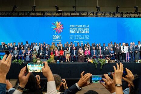 A large group of people on a stage, having their photograph taken on smartphones by people in the audience.