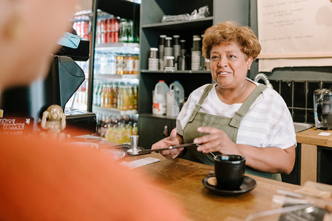 A woman behind the counter at a cafe, seemingly accepting an order from a customer. 