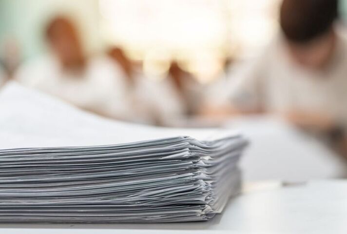 A pile of exam papers in front of some students sitting an exam