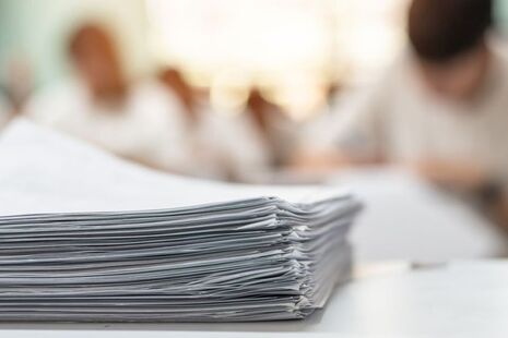 A pile of exam papers in front of some students sitting an exam