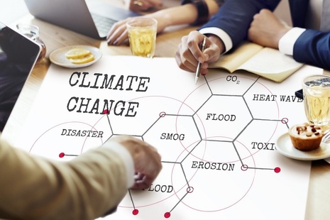 People sitting round a table looking at a chart on which are written words such as climate change, toxic, heatwave, flood and erosion.