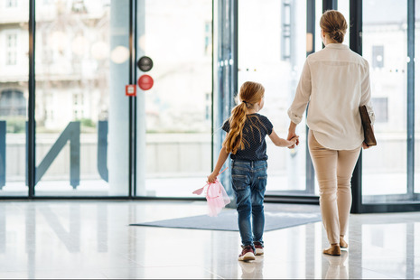 A rear view of a woman with small daughter walking in office building, holding hands.