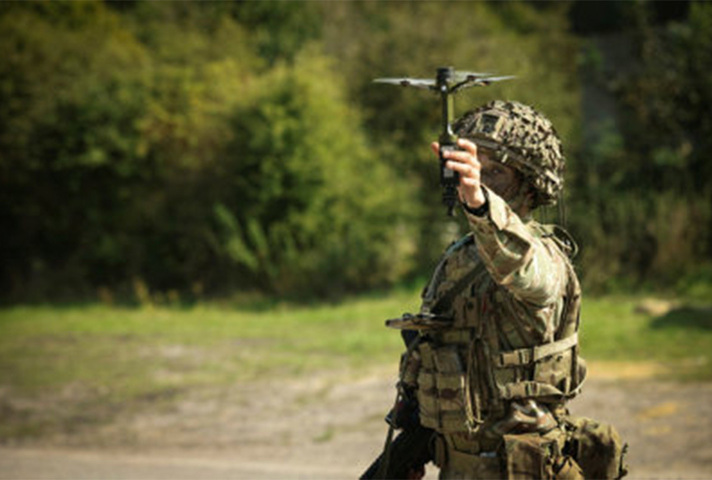 A soldier in camouflage and helmet launches a small drone.
