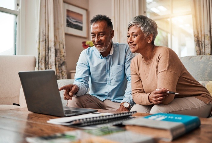 Mature couple sitting on sofa looking at laptop. Credit: iStock Photo