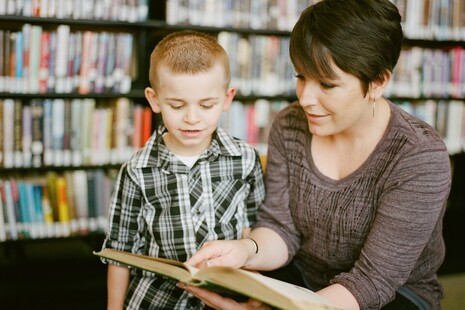 teaching assistant with a boy pupil in the school library looking at a book