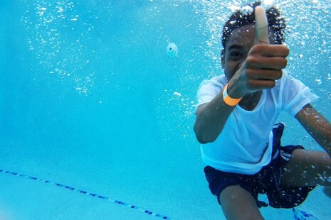 young boy swimming underwater with a thumbs up