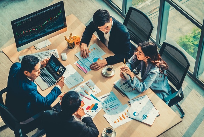 4 business people sit at table analysing data, Credit: iStock Photo