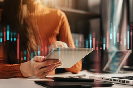 A woman holding a tablet device sat at a desk. There is overlayed graph imagery.