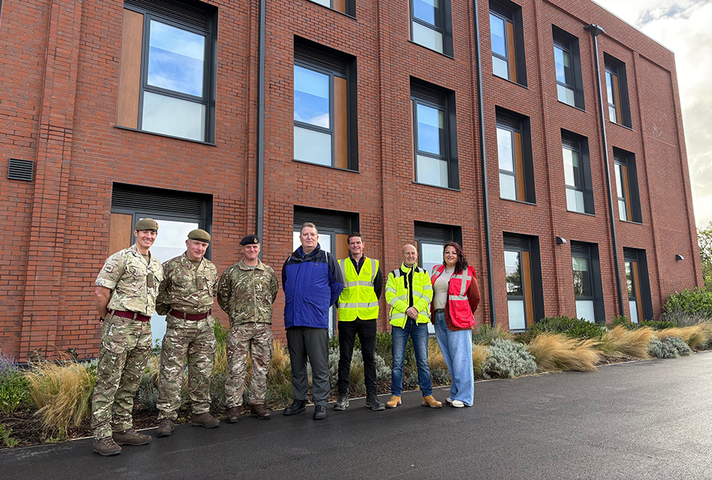 Representatives from the Army and other organisations involved standing in front of the new SLA block, a large brick building, at Weeton Barracks. 