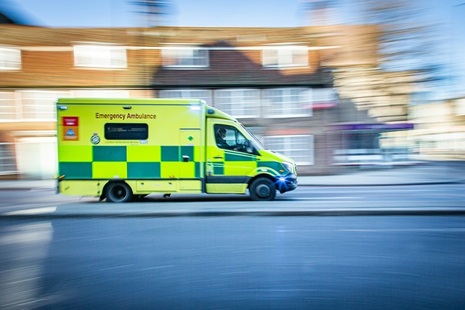 Ambulance in front of a blurred image of buildings. Credit: Unslash