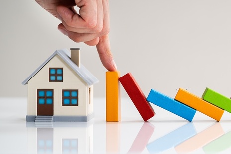 A hand from above stopping dominos hitting a wooden house