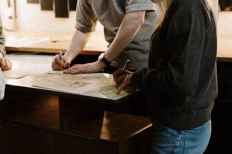 Three people standing around a table, writing on documents and notes during a collaborative work session