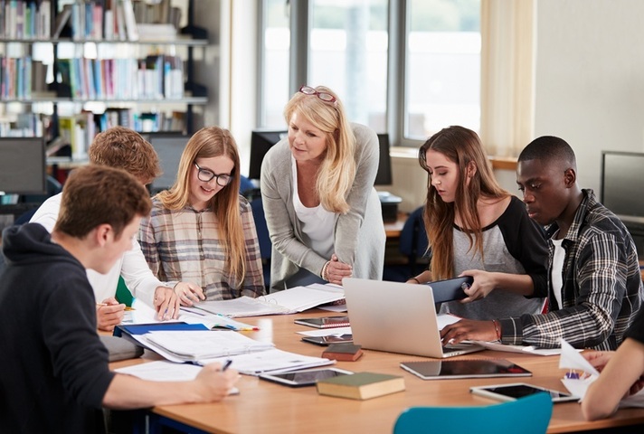 Teacher working with a group of students around a table. Credit Unsplash